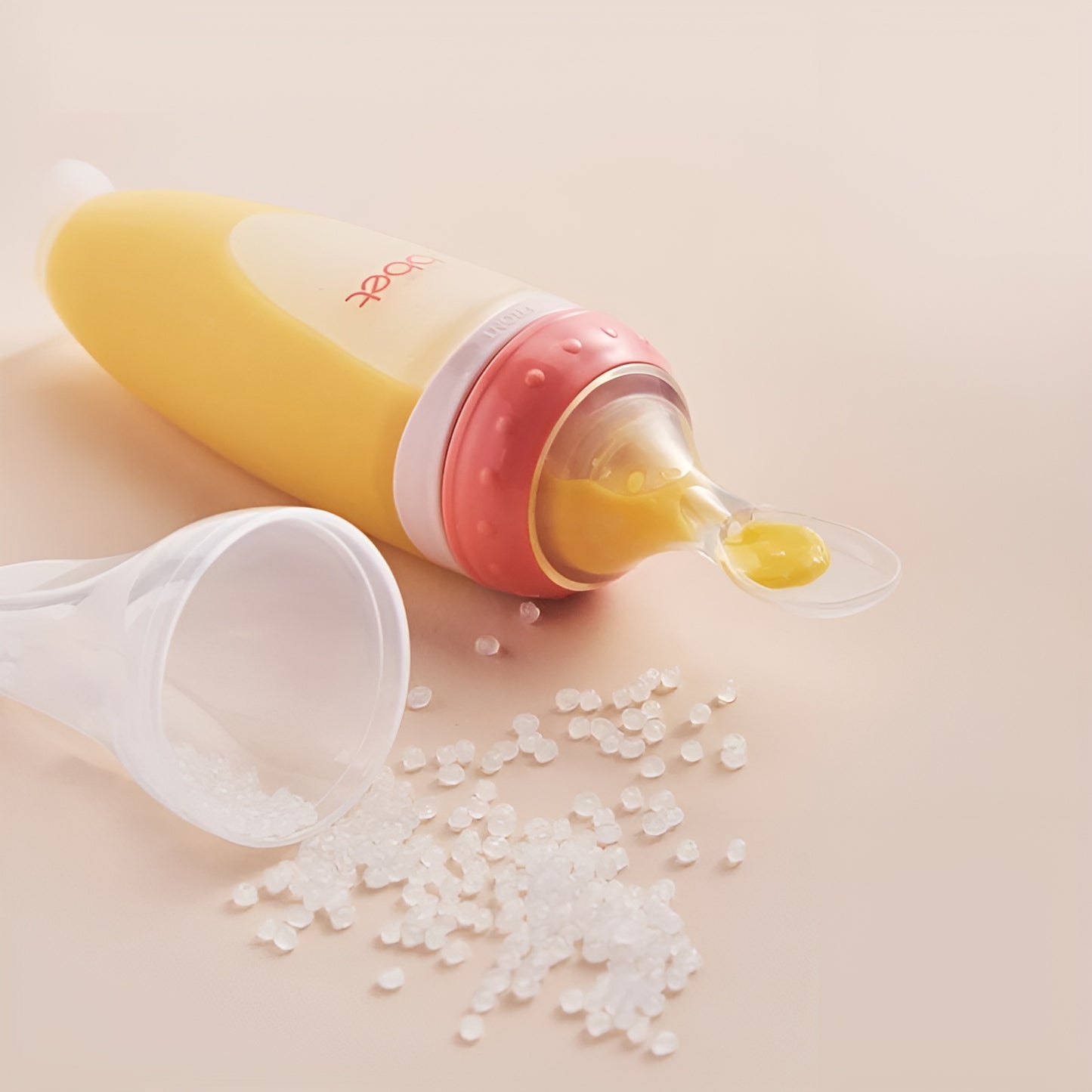 BabyHap™ Lepel-Knijpfles gevuld met gele voeding ligt naast een open plastic bakje met gemorste korrels.