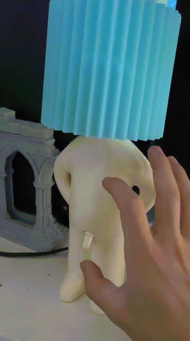 Een hand schakelt de Naughty Glow Guy™ in door de ondeugende schakelaar te gebruiken, terwijl de blauwe lampenkap een warme gloed verspreidt. Voeg humor en stijl toe aan je ruimte! Meer info op Inicala.nl.