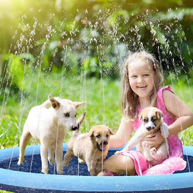 Een meisje in een roze jurk geniet lachend op de SplashPad™ FonteinMat samen met drie speelse puppy's, omringd door zachte waterstralen die verkoeling bieden op een zonnige dag. Perfect voor kinderen en huisdieren om samen plezier te hebben. inicala.nl