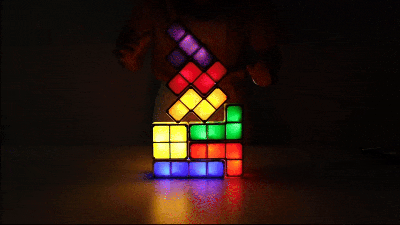 Een levendige GIF van TetraGlow™-lichtblokken die worden gestapeld in een donkere ruimte, waarbij kleurrijke LED-lichten oplichten in verschillende patronen. Een perfecte mix van nostalgie en creativiteit in actie! inicala