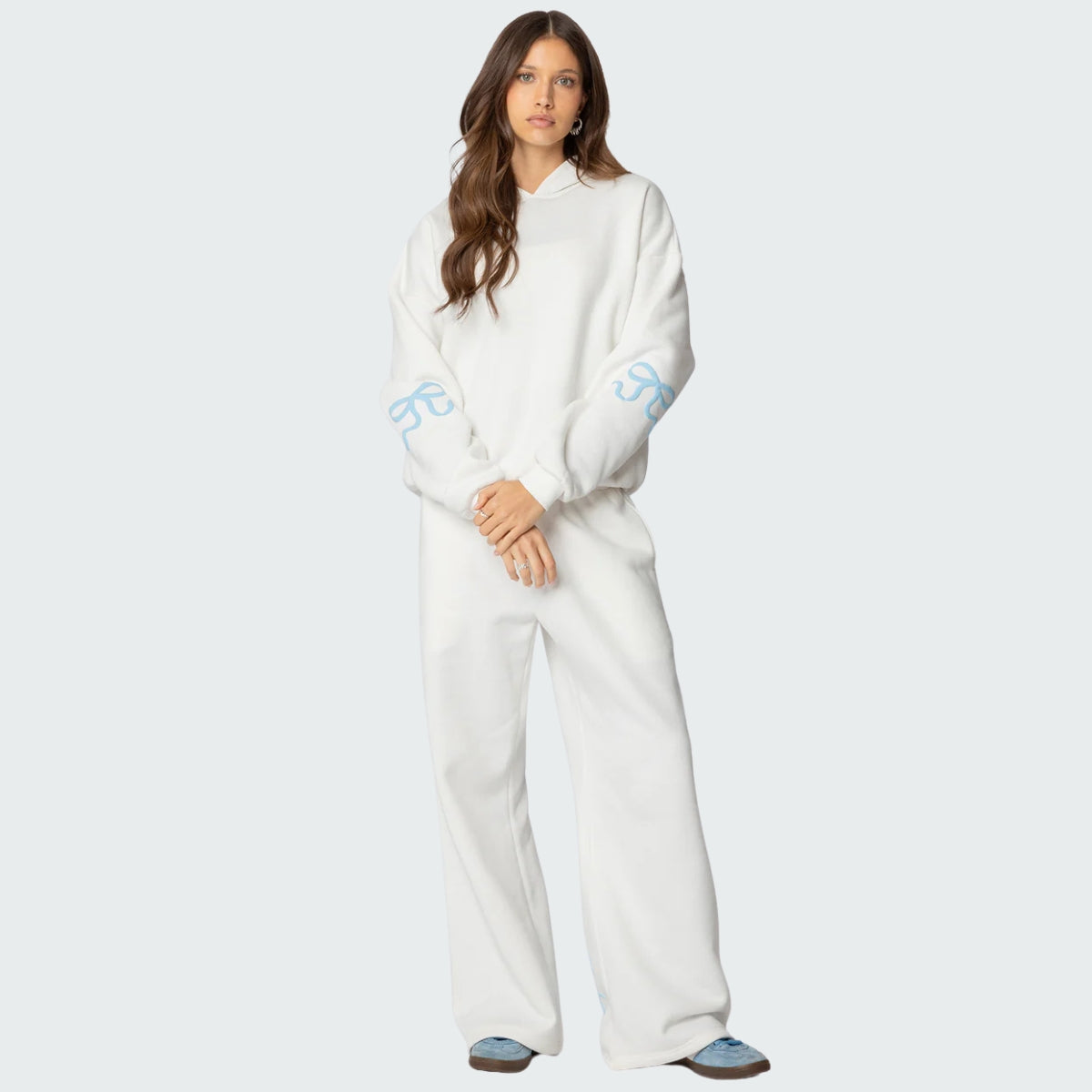 Luna Ribbon Tracksuit - Elegantie in Comfort Witte hoodie en broekset met luchtige pasvorm, gedecoreerd met blauwe strikdetails op mouwen en broek. Perfect voor stijl en comfort. Exclusief verkrijgbaar via Inicala.nl.