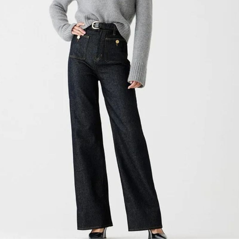 Model draagt de Riviera Flare™ jeans in donkere denim van Inicala.nl, met hoge taille, brede pijpen en gouden knoopdetails – een elegante en flatterende fit met Franse flair voor elke dag.