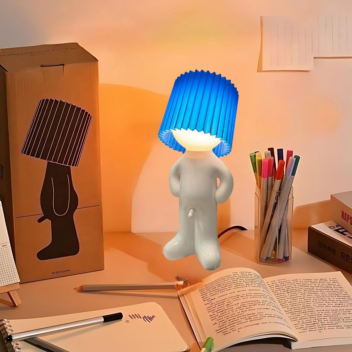 Naughty Glow Guy™ Grappig, brutaal, met een grenzeloze glimlach! Een ondeugende lamp met een opvallende blauwe kap, omgeven door een kleurrijke werkruimte. Voeg een speelse twist en verlichting toe aan je interieur. Meer ontdekken Bezoek Inicala.nl.