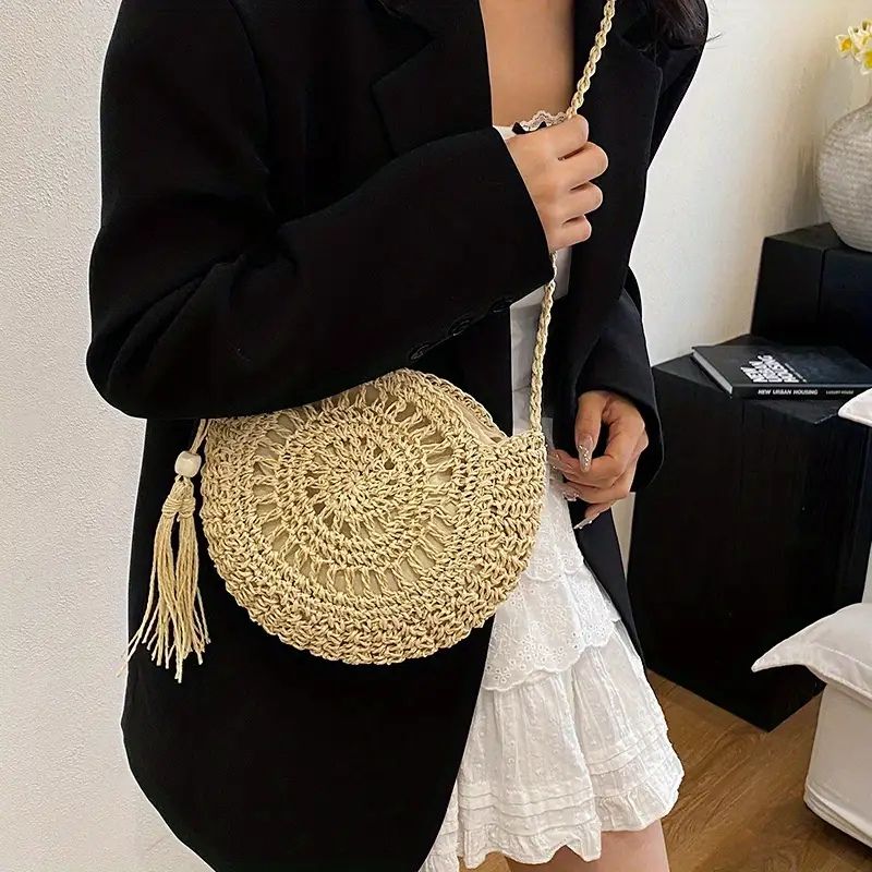 SolaraBoho™ – Ronde handgemaakte gevlochten crossbody tas in naturel, gedragen door een vrouw met witte jurk en zwarte blazer. Inicala.nl, stijlvol boho accessoire.