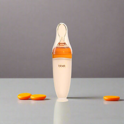 BabyHap™ Lepel-Knijpfles met Oranje en witte accenten op een ondergrond. De fles is ideaal voor stressvrij voeden, gemaakt van voedselveilige siliconen en eenvoudig schoon te maken.