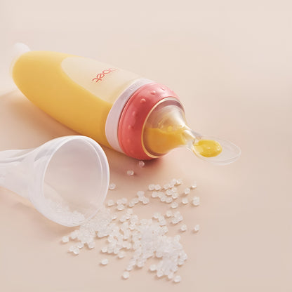 BabyHap™ Lepel-Knijpfles gevuld met gele voeding ligt naast een open plastic bakje met gemorste korrels.
