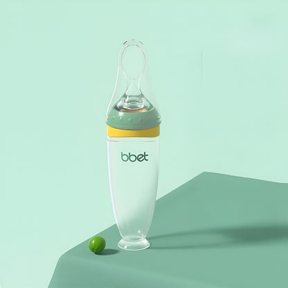 BabyHap™ Lepel-Knijpfles met groene en gele accenten op een groene ondergrond. De fles is ideaal voor stressvrij voeden, gemaakt van voedselveilige siliconen en eenvoudig schoon te maken.