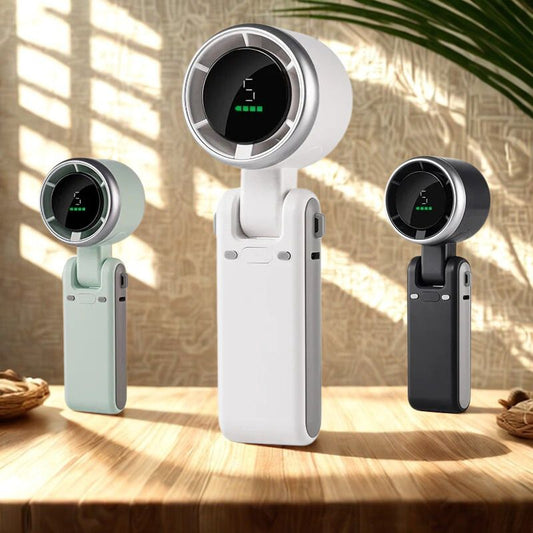 Drie BreezeBuddy™ ventilators op een houten tafel in zonlicht – wit, mintgroen en zwart model. Compact design met HD-display. Verkrijgbaar op Inicala.nl.