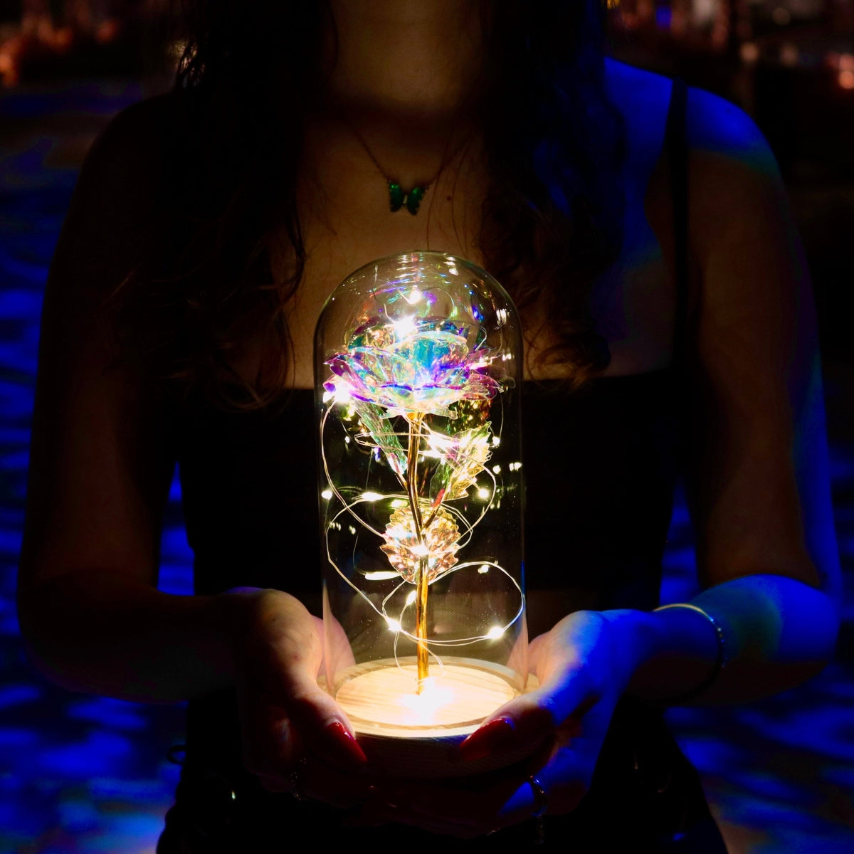 Inicala: Een vrouw houdt een verlichte glazen stolp vast met daarin een sprankelende roos en warme LED-lichtjes. Dit unieke en magische decorstuk straalt elegantie en liefde uit.
