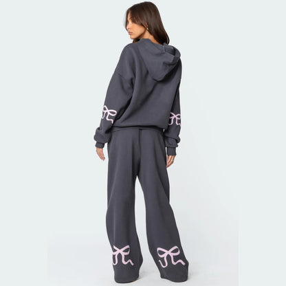 Luna Ribbon Tracksuit - Elegantie in Comfort Donkergrijze broek met wijde pijpen, versierd met subtiele roze strikdetails. Perfect voor een moeiteloze, stijlvolle look. Shop nu op Inicala.nl en ervaar ultiem comfort met ee