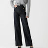 Model draagt de Riviera Flare™ jeans in donkere denim van Inicala.nl, met hoge taille, brede pijpen en gouden knoopdetails – een elegante en flatterende fit met Franse flair voor elke dag.