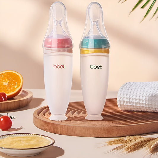Twee BabyHap™ Lepel-Knijpflessen, één met roze en één met groene schroefdop, staan rechtop op een houten bord, omringd door een sinaasappel, tomaten en een witte handdoek, klaar voor gebruik.